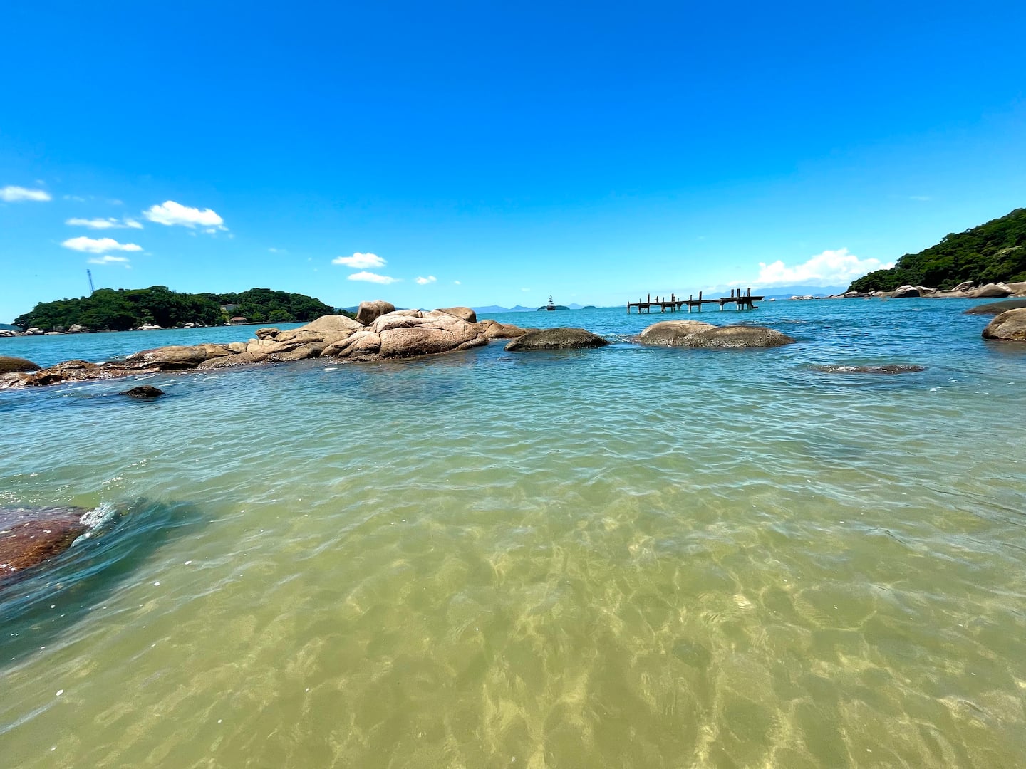 Água transparente sobre a areia e pedras ao fundo